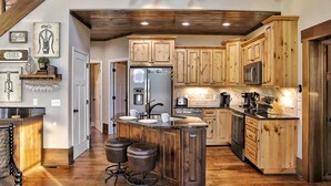 A spacious kitchen with wooden cabinets, a central island with stools, and a stainless steel refrigerator.
