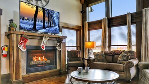 A cozy living room with a fireplace, a television mounted above it, and a large window providing natural light.