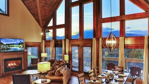 A spacious living room with a fireplace, large windows, and a dining area set for a meal.