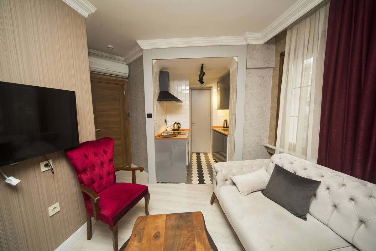 A living room with a red chair, a white sofa, a wooden coffee table, and a flat-screen TV mounted on the wall.