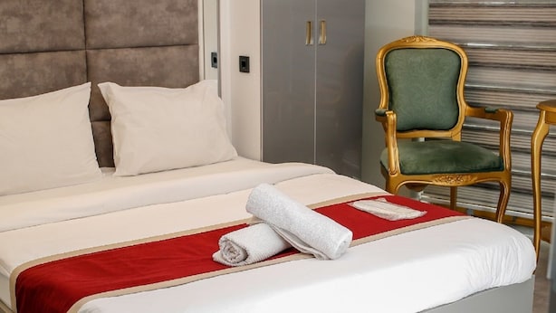 A modern hotel room with a large bed, a green upholstered chair, and a large window with blinds. - Hermes Park Hotel Sisli (Istanbul)