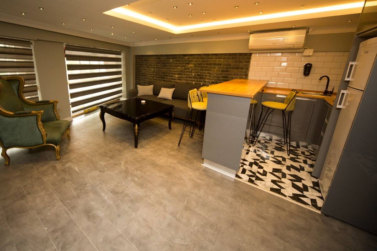 A modern kitchen with a bar area, a dining set, and a green armchair.