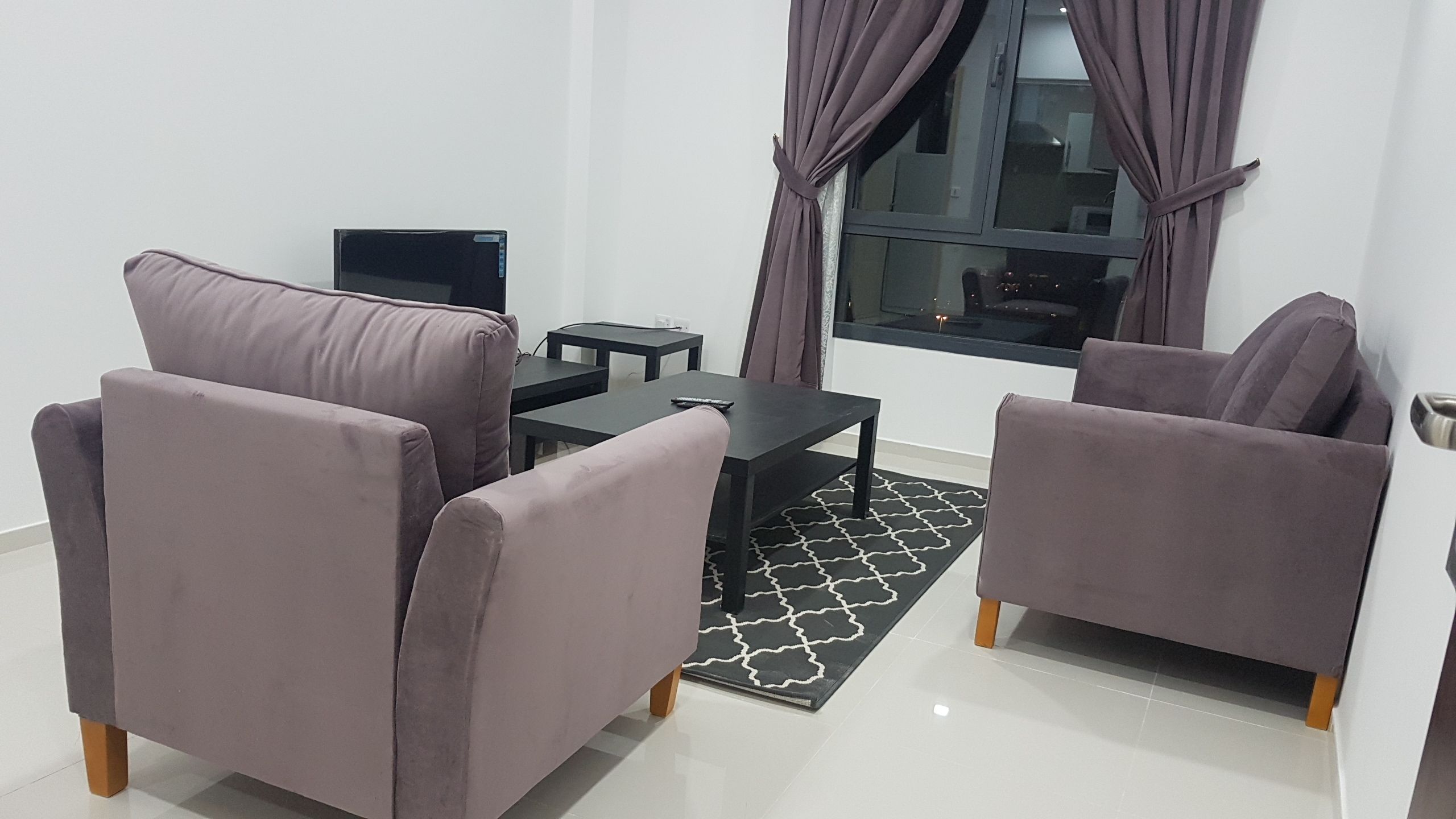 A modern living room with two grey sofas, a black coffee table, and a TV on a stand.