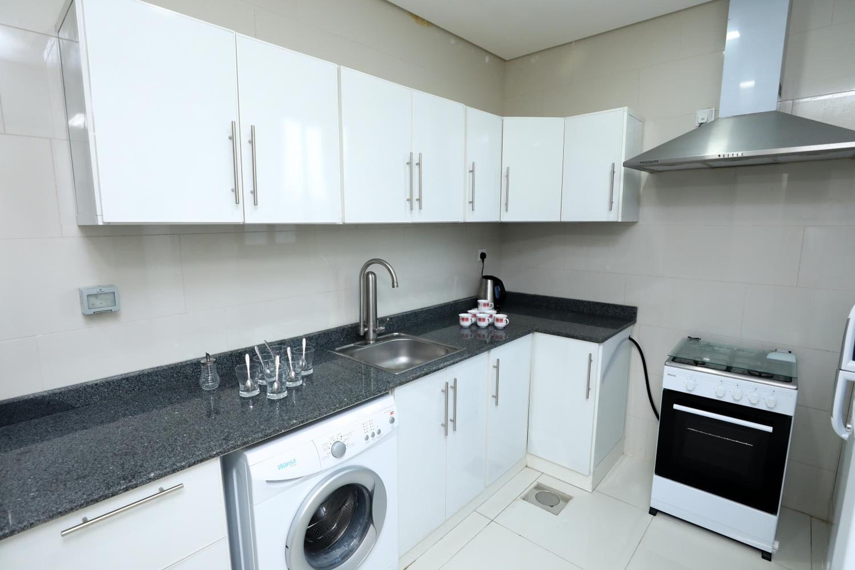 Une cuisine compacte avec des meubles blancs, un évier en acier inoxydable, un lave-linge et une cuisinière.