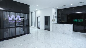 Un moderno vestíbulo de hotel con una recepción, un muro de cristal con un letrero que dice "Magic Suite" y un suelo de mármol.