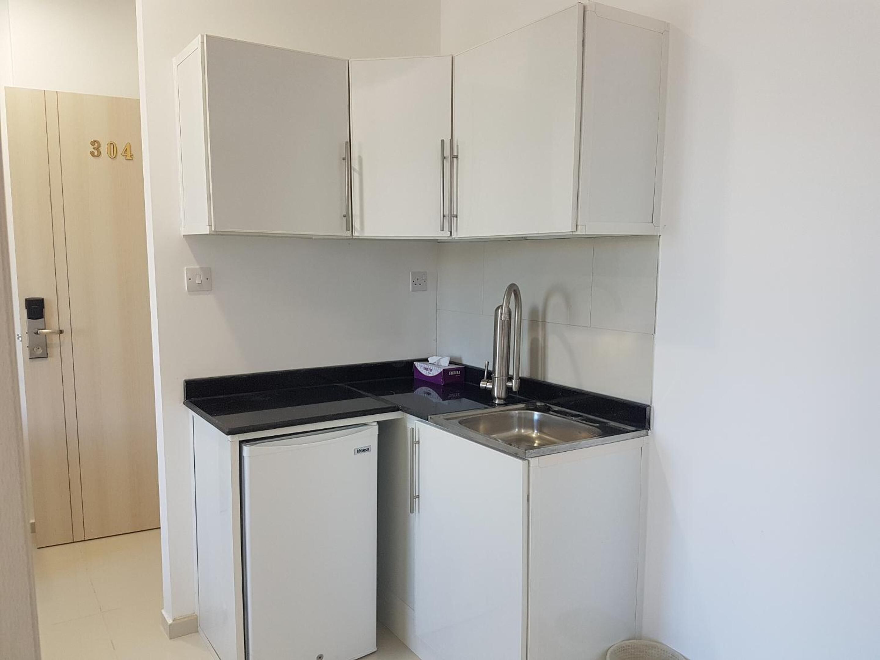 Una cocina compacta con armarios blancos, un refrigerador pequeño y un lavamanos.