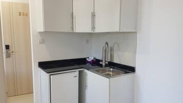 Una cocina compacta con armarios blancos, un refrigerador pequeño y un lavamanos.