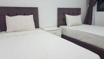 A hotel room with two beds, each with a headboard and a pillow. There is a nightstand between the beds.