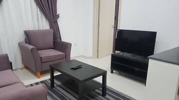 A living room with a sofa, a coffee table, a TV stand, and a door.