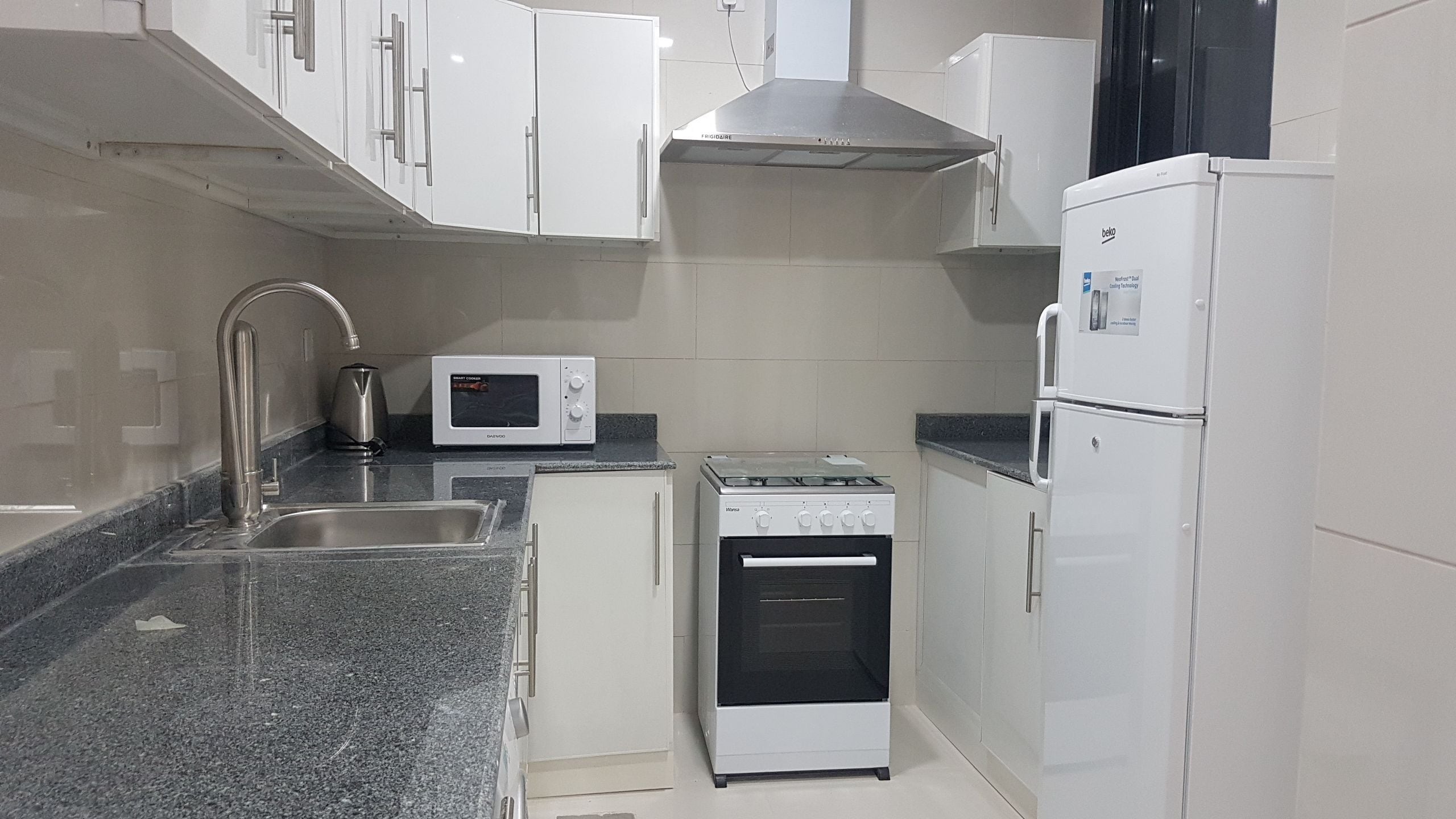 A compact kitchen with white cabinets, a stainless steel sink, a microwave, a stove, and a refrigerator.