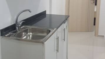 Cozinha com armários brancos, pia de aço inoxidável e bancada preta.