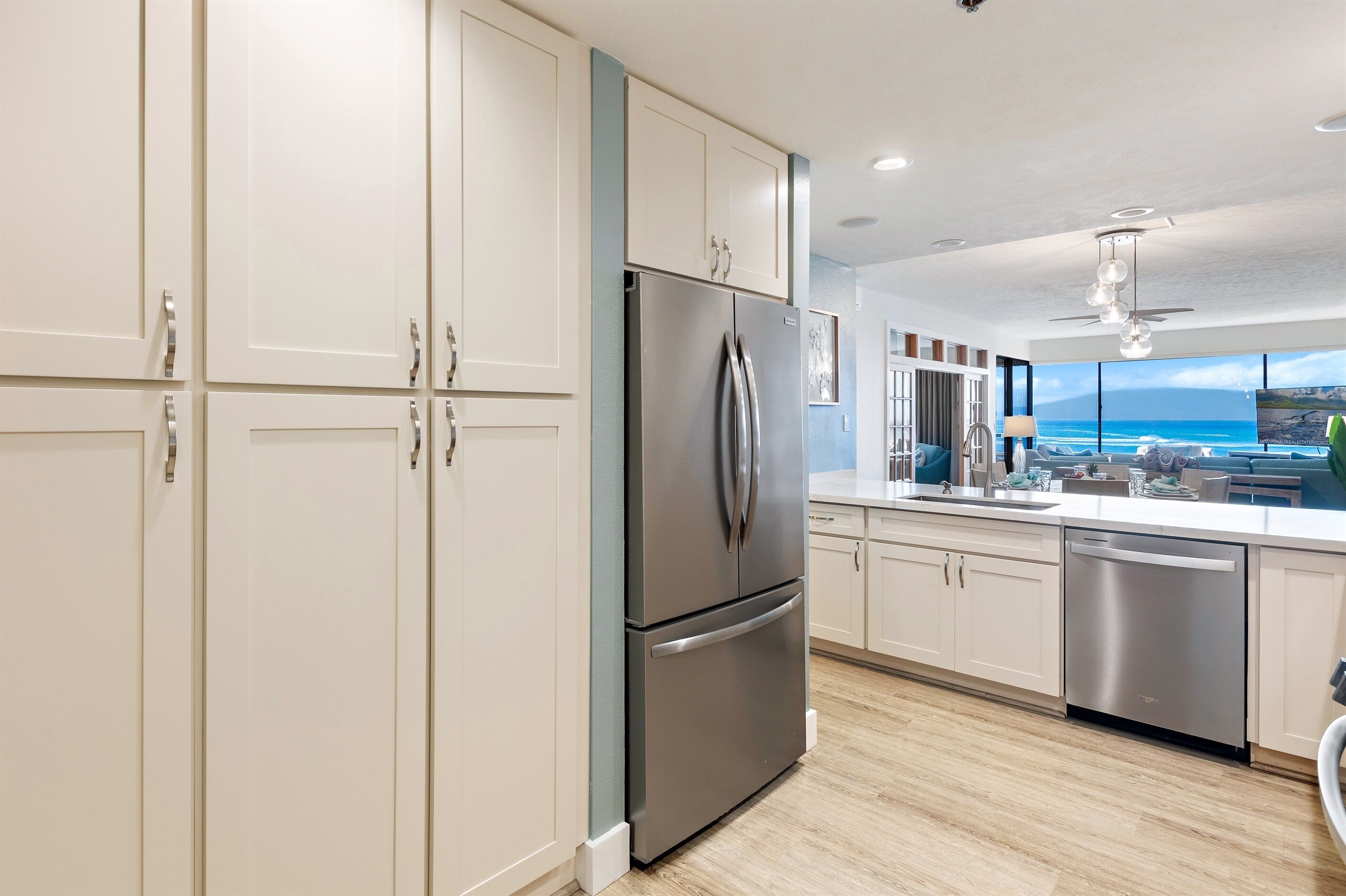 A modern kitchen with stainless steel appliances, white cabinetry, and a view of the ocean.
