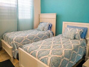 Two single beds with matching headboards and footboards, a window with blinds, and a teal wall.