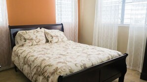 A bed with a patterned bedspread in a room with orange walls and a window with sheer curtains.