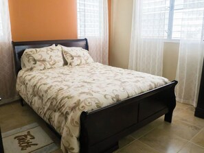 Een bed met een bloemenprintdeken in een kamer met oranje wanden en een raam met gordijnen.