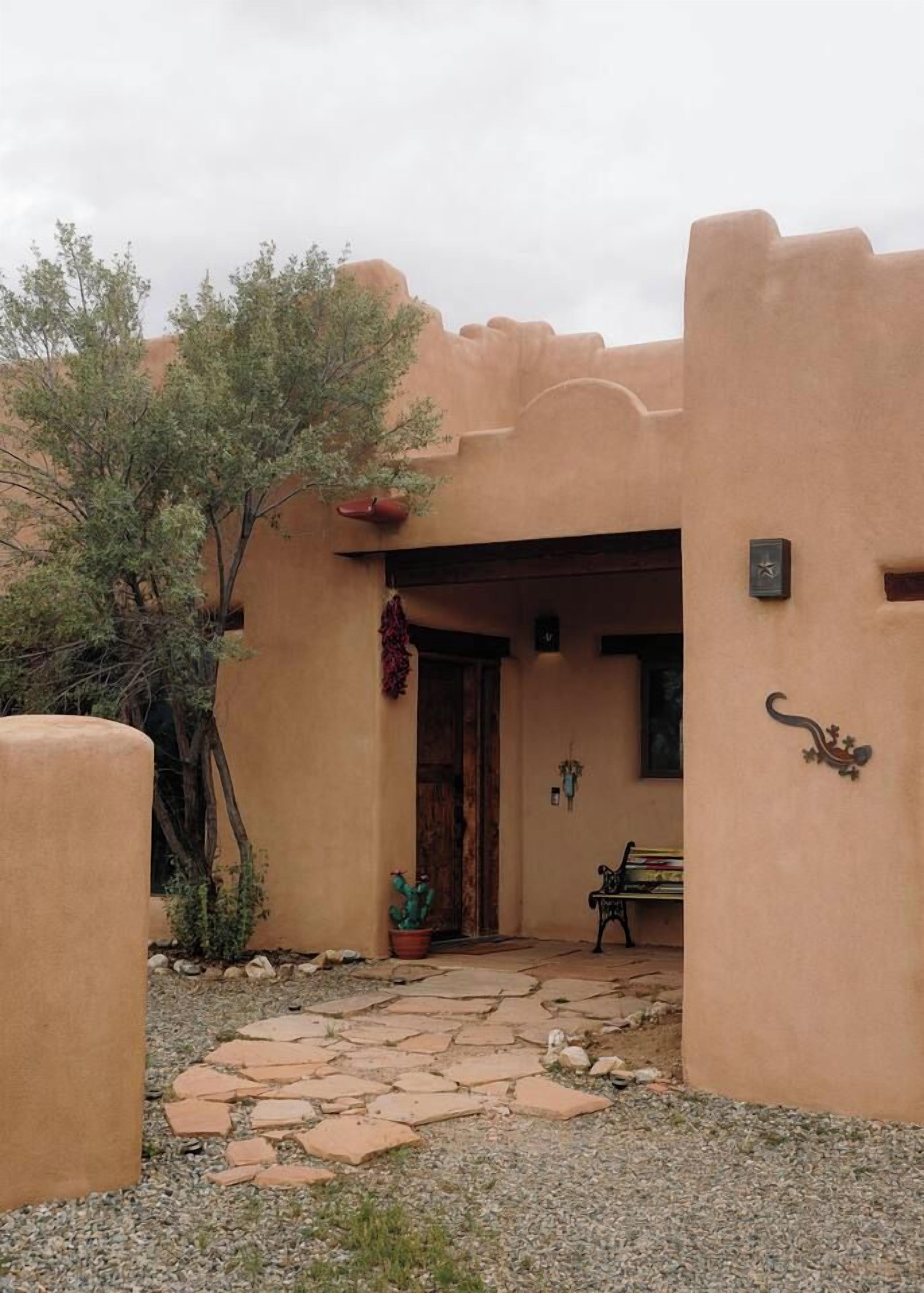 A building with a stone pathway leading to a wooden door, surrounded by a low wall and a tree.