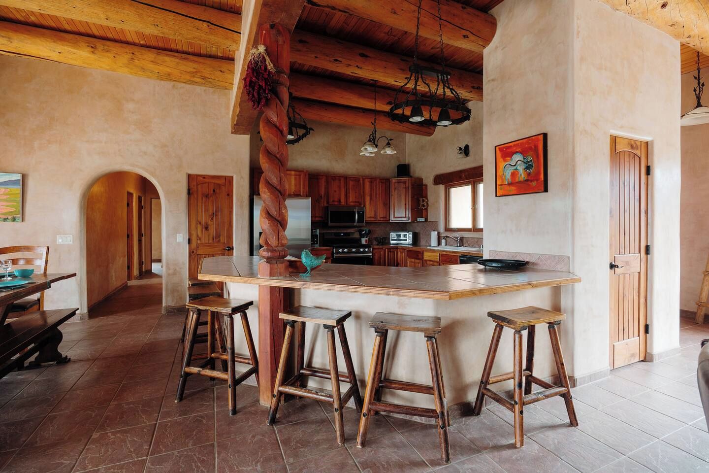 A kitchen with a central island, wooden stools, and a rustic ceiling.