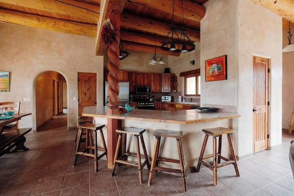 A kitchen with a central island, wooden stools, and a rustic ceiling.