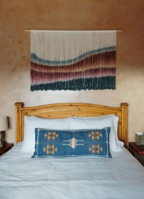 A bed with a wooden headboard, a white pillow, and a blue pillow with a geometric pattern.