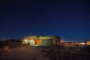 A single-story building with a garage, surrounded by dry vegetation, under a starry night sky.