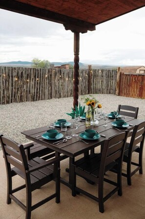 Une table en bois installée à l’extérieur, avec des chaises, une clôture en bois et une vue sur des collines lointaines.