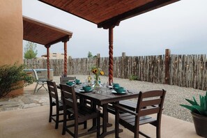 Une terrasse extérieure avec une table en bois dressée pour le repas, entourée de chaises, et une clôture en bois rustique en arrière-plan.