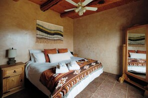 Quarto com cama, mesa de cabeceira, luminária, ventilador de teto e espelho.