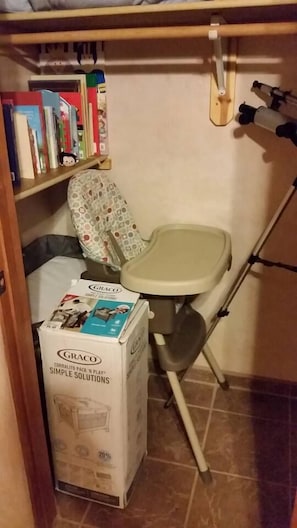 Um banheiro pequeno com vaso sanitário, uma prateleira com livros e um assento de bebê Graco.