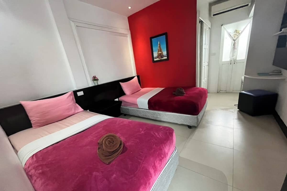 A hotel room with two beds, a red accent wall, a framed picture, and a window with curtains.