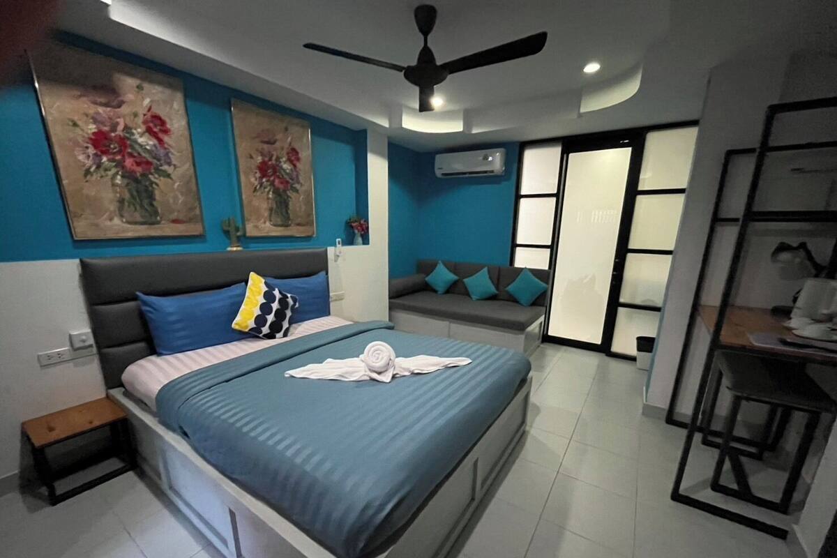 A modern bedroom with a bed, a ceiling fan, a sofa, and a dining area.