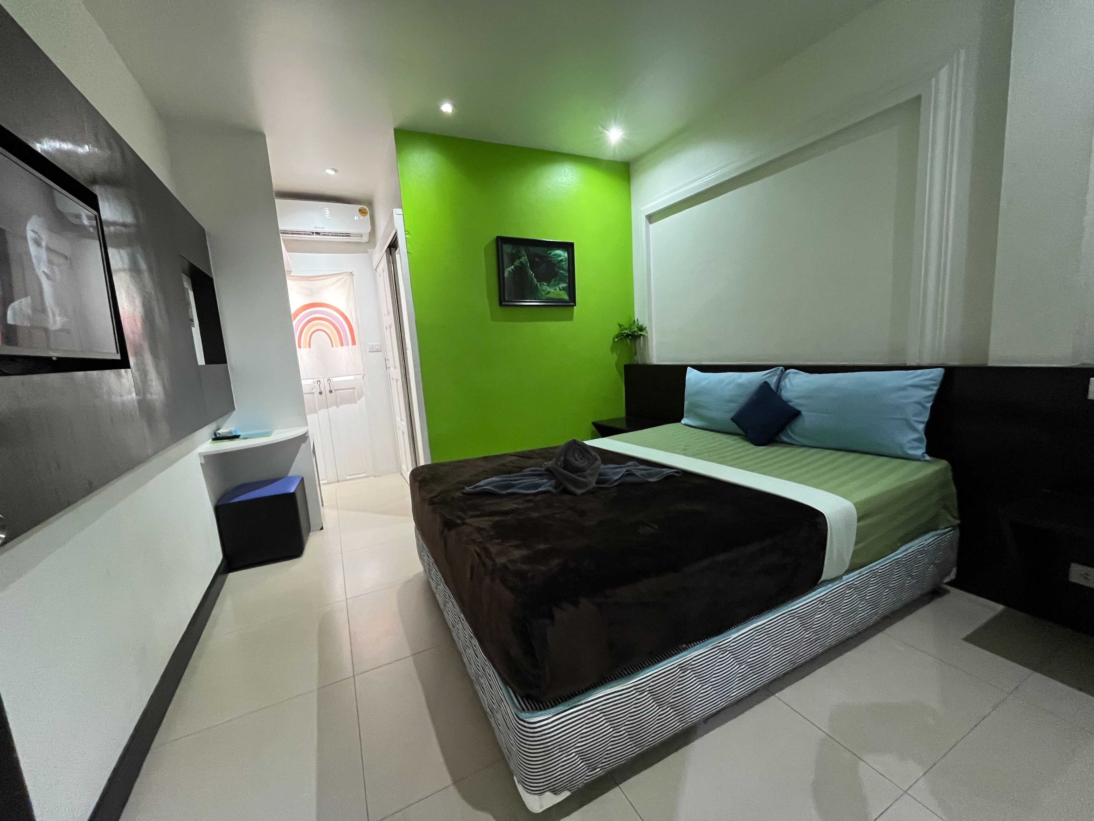 Une chambre à coucher avec un lit, une télévision, un mur vert et une porte donnant sur une autre pièce.
