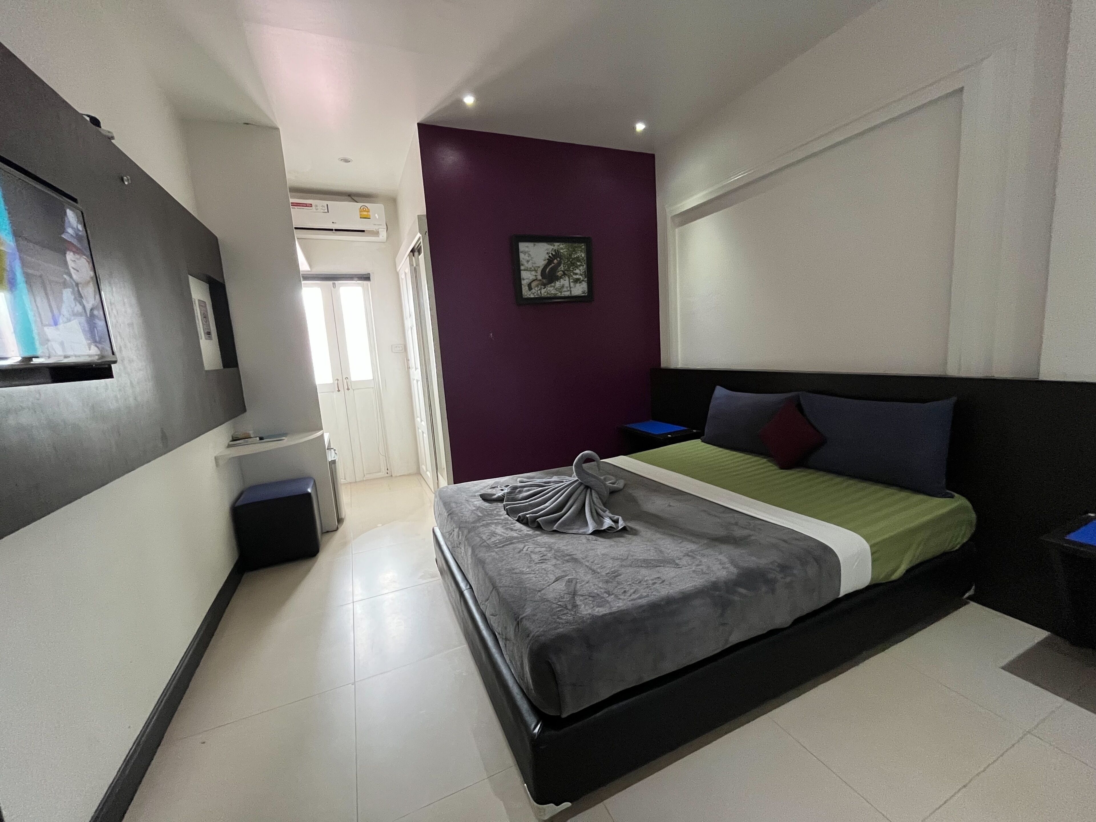 Ein modernes Hotelzimmer mit einem Bett, einem kleinen Nachttisch, einer Wand-Klimaanlage und einer Tür zu einem weiteren Raum.