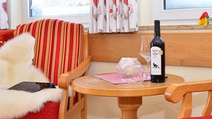 A cozy seating area with striped red and white cushions, a wooden table with a wine bottle and glass, and a decorative vase with flowers.