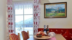 A dining area with a wooden table, red upholstered booth seating, and a window with a view of snow-covered mountains.