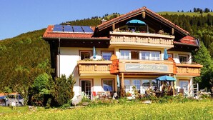 A two-story building with a sign reading "Landhaus Hubert's Hide" and a balcony with outdoor seating.