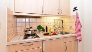 A kitchen with light wooden cabinets, a stainless steel sink, and a variety of kitchen utensils hanging on the wall.