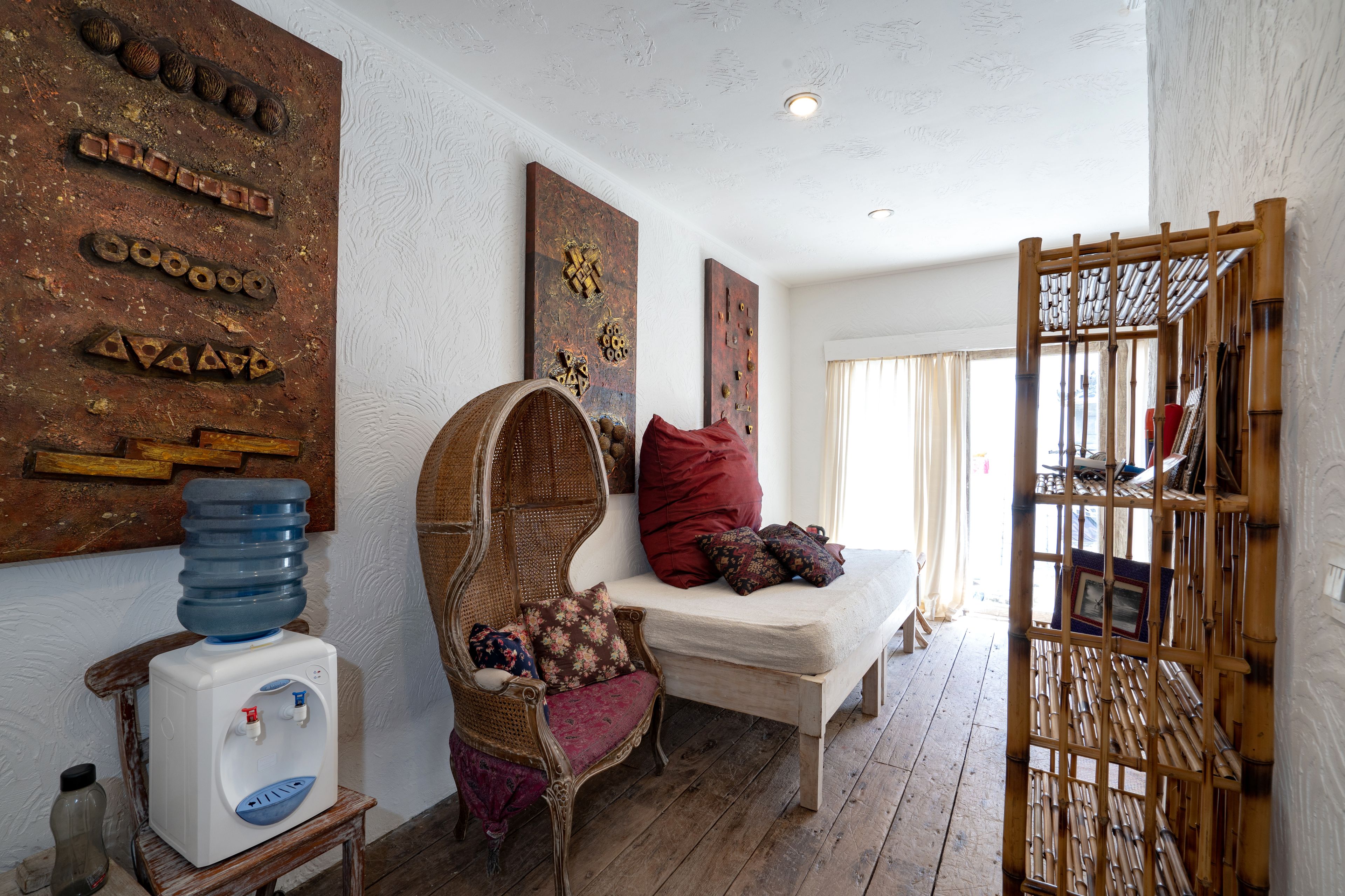 A room with a wooden bench, a wicker chair, and a water dispenser.