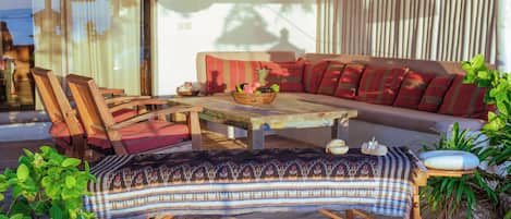 Uma área de estar externa aconchegante com mesa de madeira, cadeiras e um sofá.