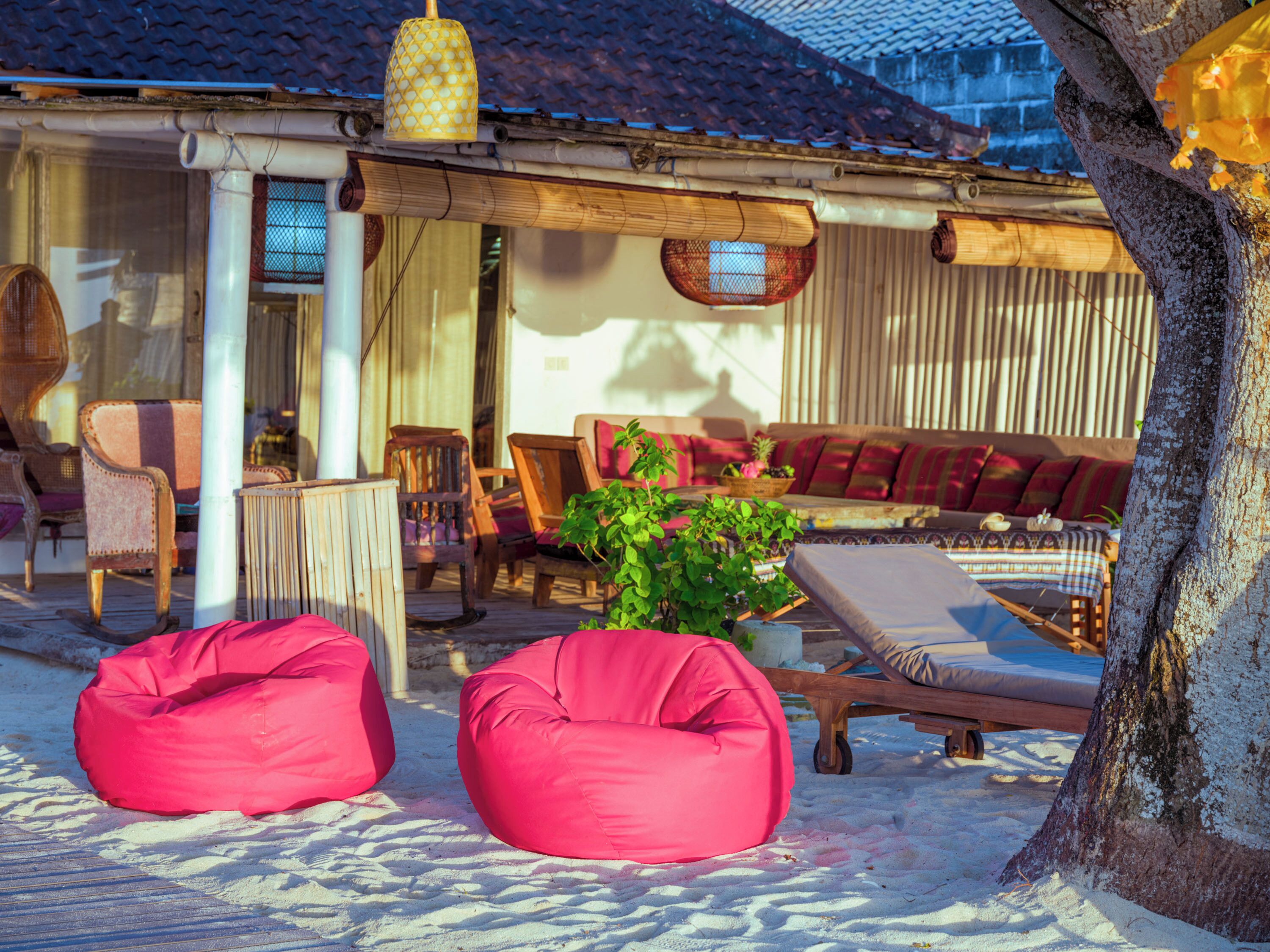 A beachside lounge with a wooden deck, lounge chairs, and a seating area with cushions.
