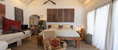 Een ruime slaapkamer met een groot bed, een houten stoel en een plafondventilator.