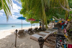 A beach with lounge chairs and umbrellas, a palm tree, and a view of the ocean. - Villa Pasir (Lembongan Island)