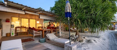 A beachside villa with a wooden deck, a lounge chair, and a dining area.