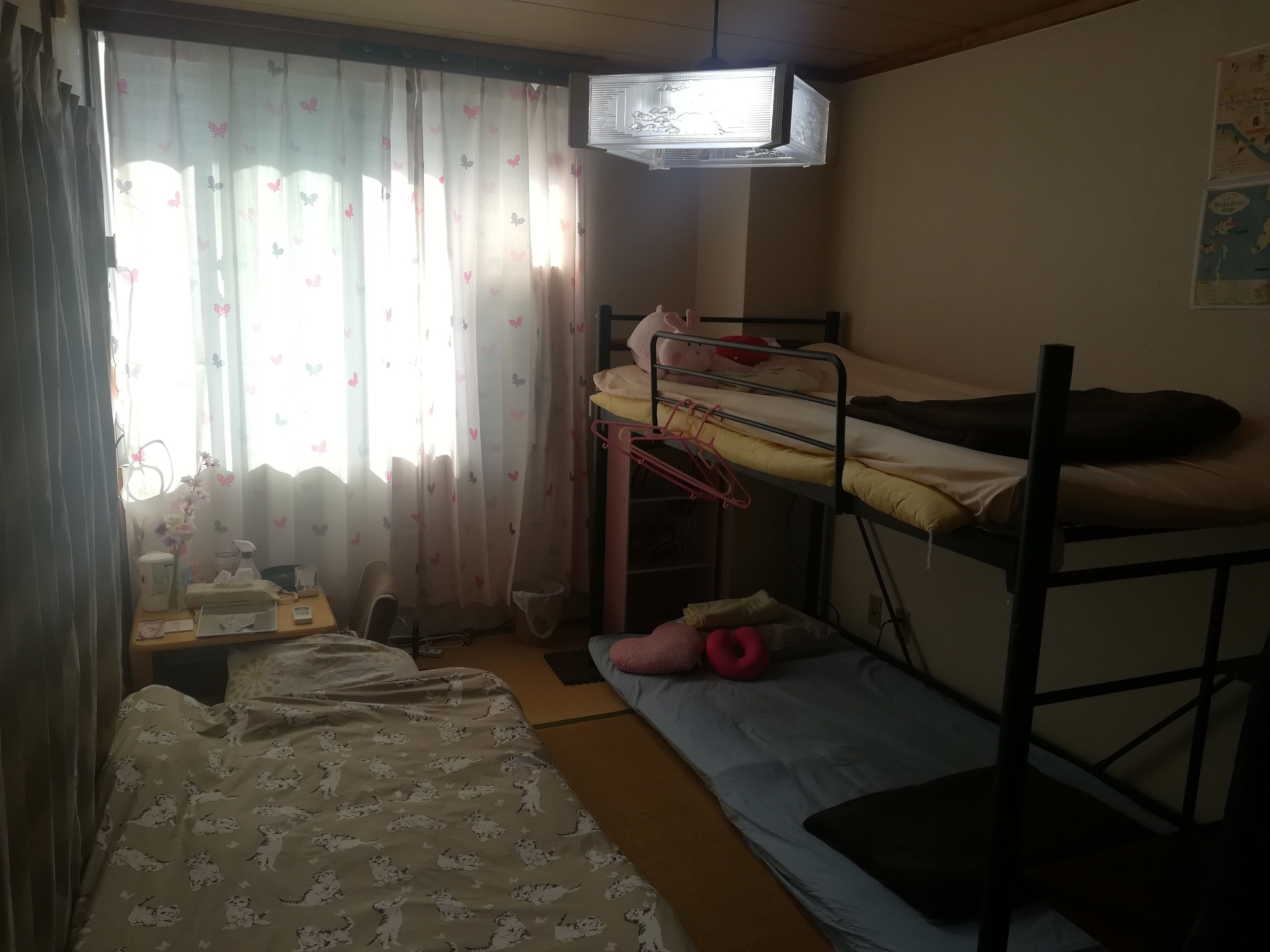 Ein Schlafsaalzimmer mit Etagenbetten, einem Schreibtisch mit Stuhl, einem kleinen Tisch und einem Fenster mit Vorhängen.