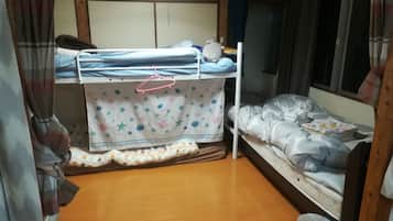 A dormitory room with bunk beds, a wooden floor, and a curtain-covered window.