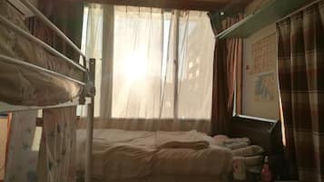 Een slaapkamer met stapelbedden, een bureau met stoel, een kaart aan de muur en een raam met dunne gordijnen.