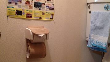 Een badkamer met toilet, een rol toiletpapier, een handdoek aan de muur en een poster met lokale attracties.