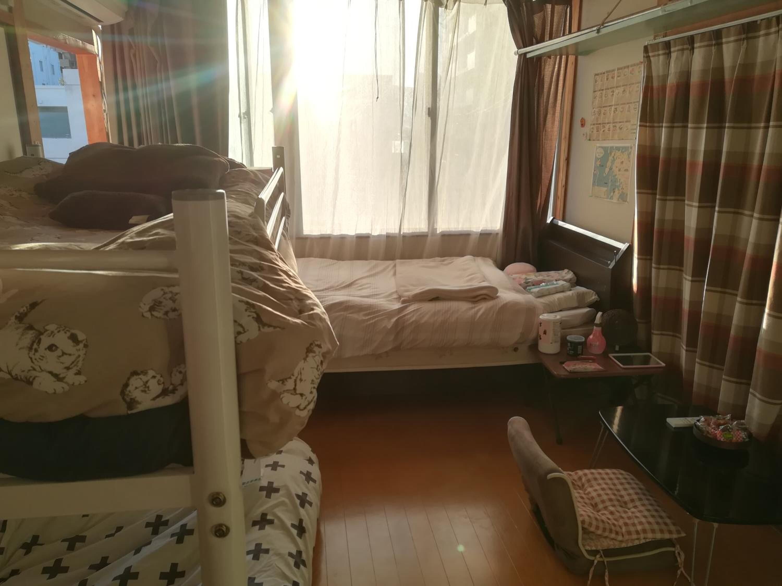 A room with two beds, a small table with a lamp, and a window with curtains.