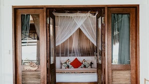 Una habitación con cama bajo un dosel, puertas de madera y vistas al exterior.