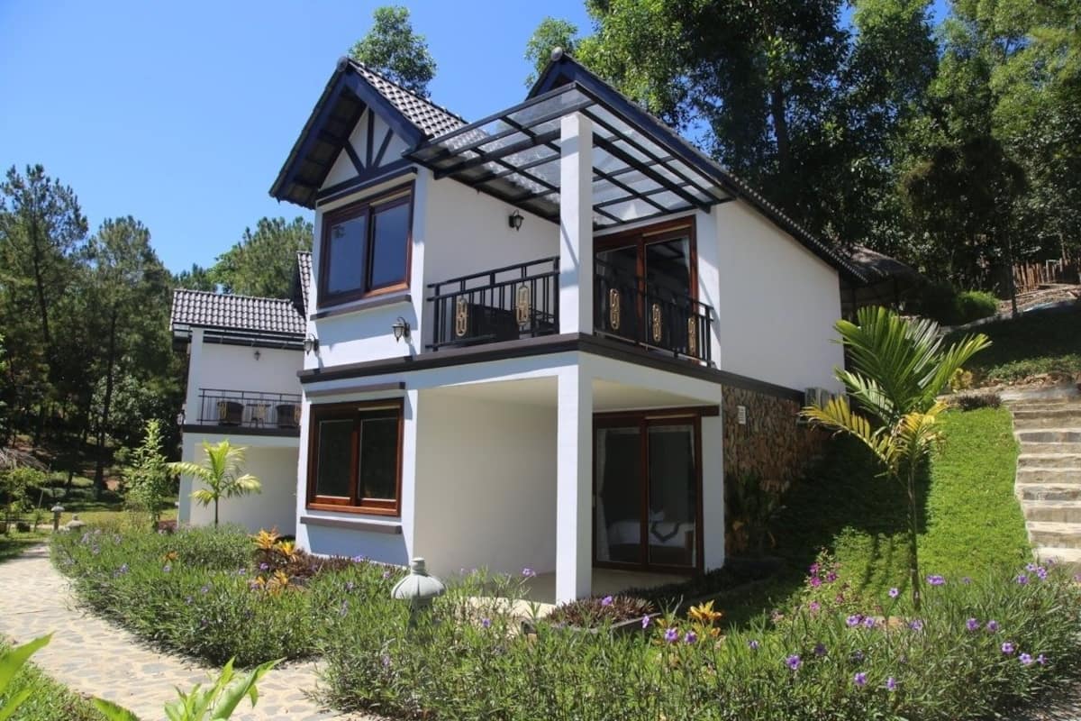 A two-story house with a balcony, surrounded by a garden with various plants and flowers.