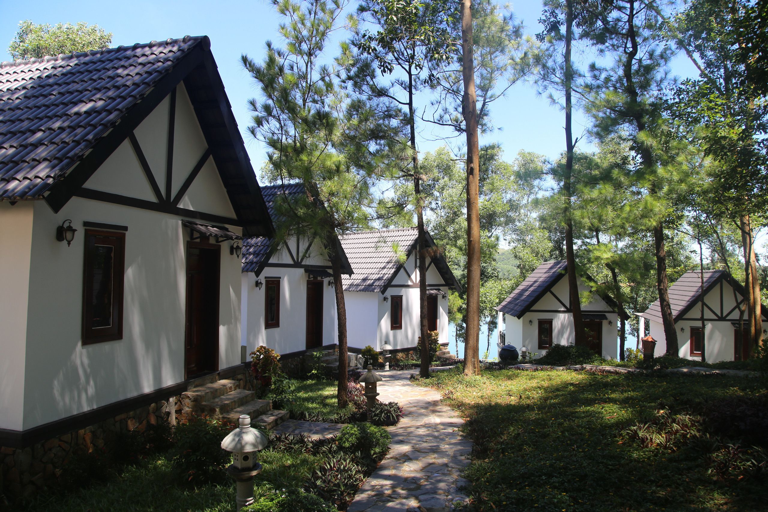 A row of traditional half-timbered houses with stone foundations and dark wooden beams, surrounded by lush greenery and tall trees.